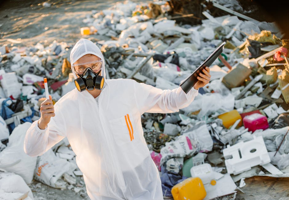 An extensive view of a large landfill site filled with a densely packed mixture of household waste, including crumpled and torn plastic packaging, paper, cardboard, and food wrappers, with scattered d